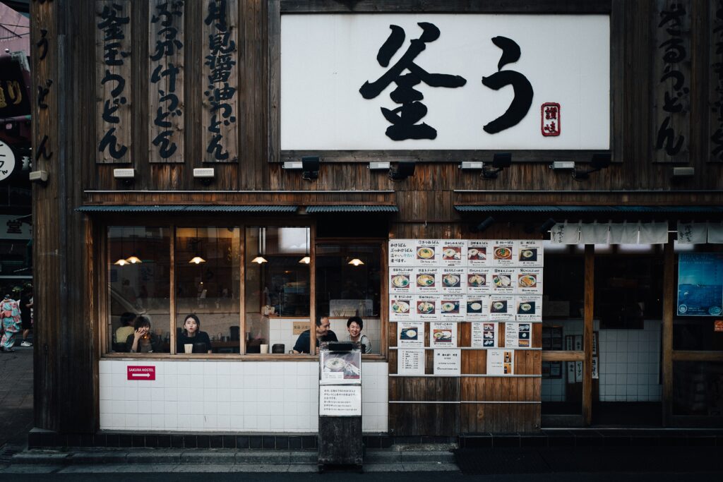 The outside of a Japanese restaurant with a menu and customers in the window