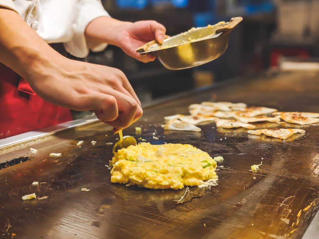 a chef makes okonomiyaki on a grill
