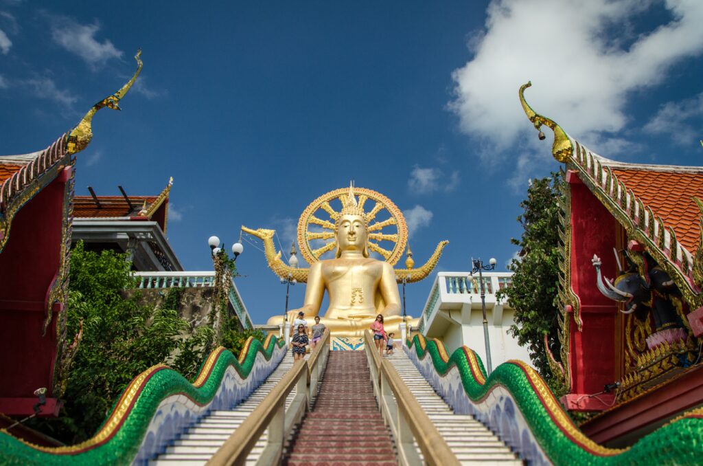 the gold big buddha sits on top of a hill with stairs leading up
